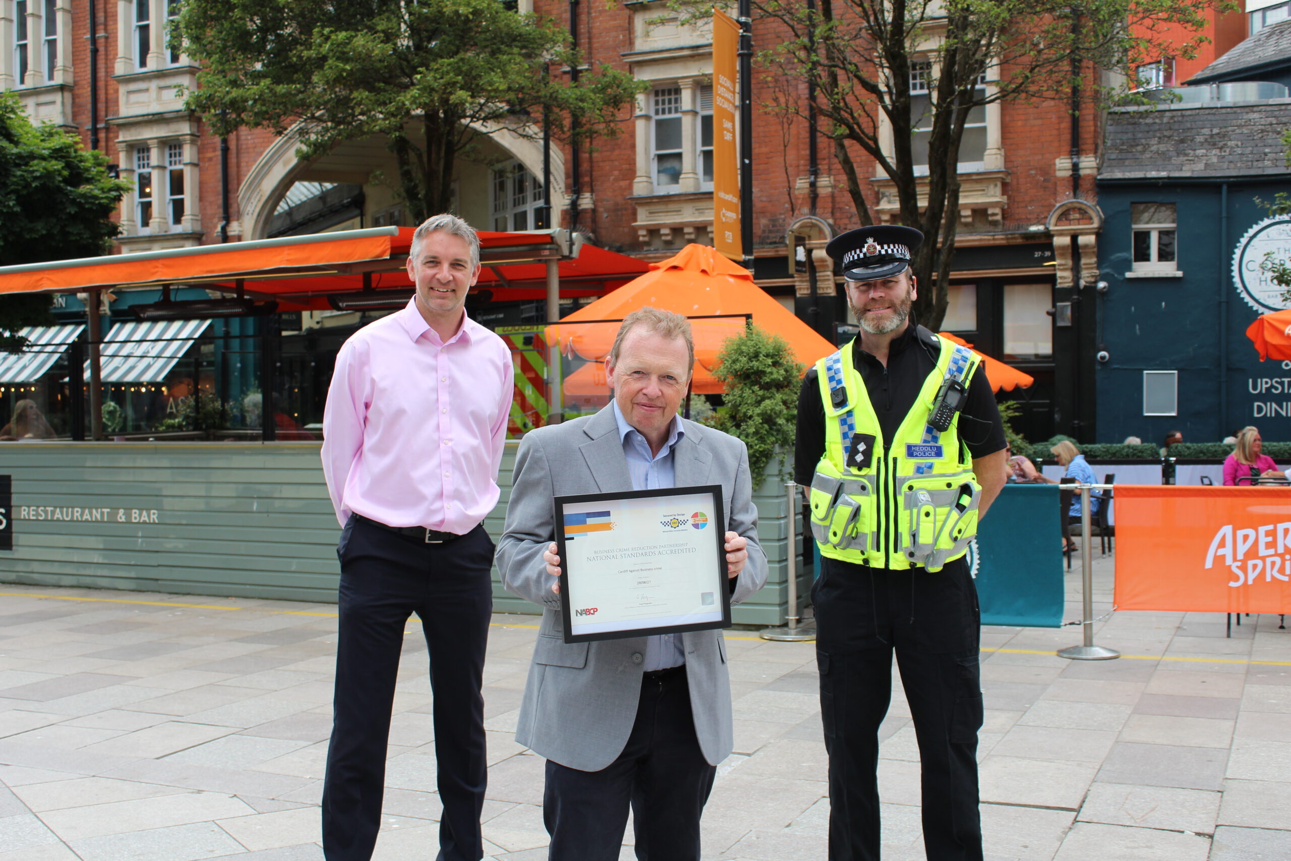 three men standing in Cardiff city centre holding the national standards accreditation certificate