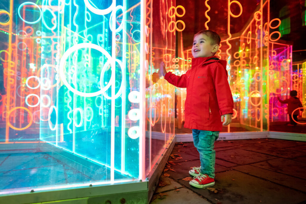 close up of little boy in red jacket looking up at the colourful light maze