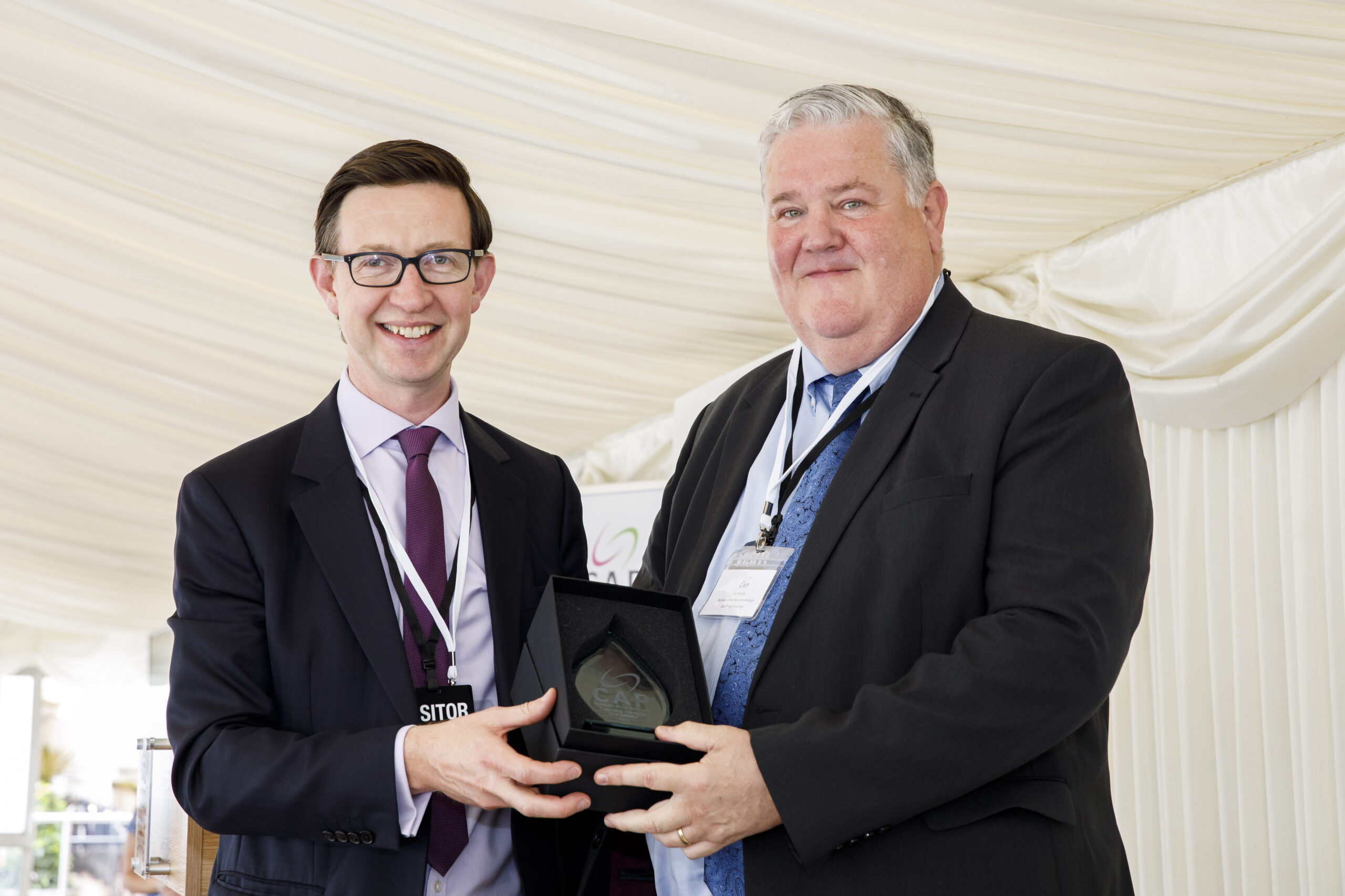 two men dressed in suits holding the CAP award