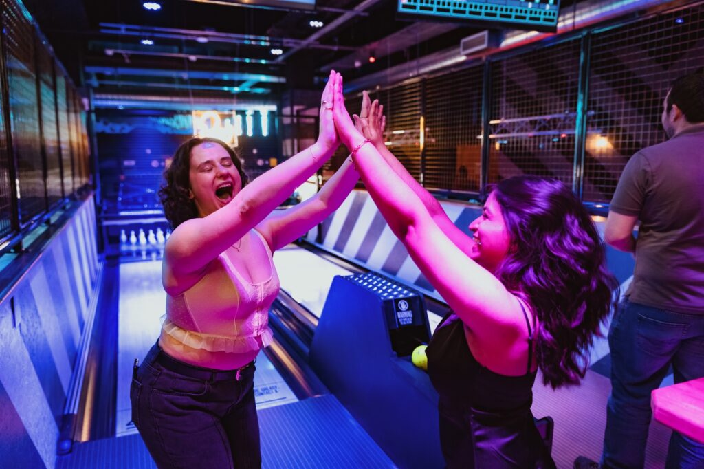 Two women high five joyfully in front of a bowling alley