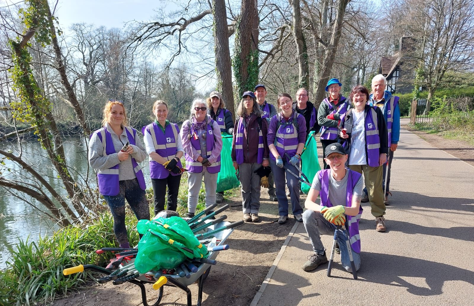Group of adults gathered in a sunny park wearing high vis jackets and holding litter picking equipment